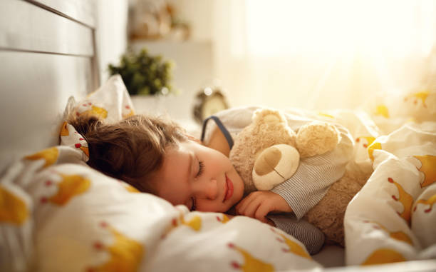 child girl sleeps in her bed with a toy teddy bear in morning
